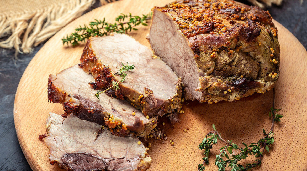 Large sliced piece of baked pork back wwith mustard and thyme on a wooden board. Food recipe background. Close up
