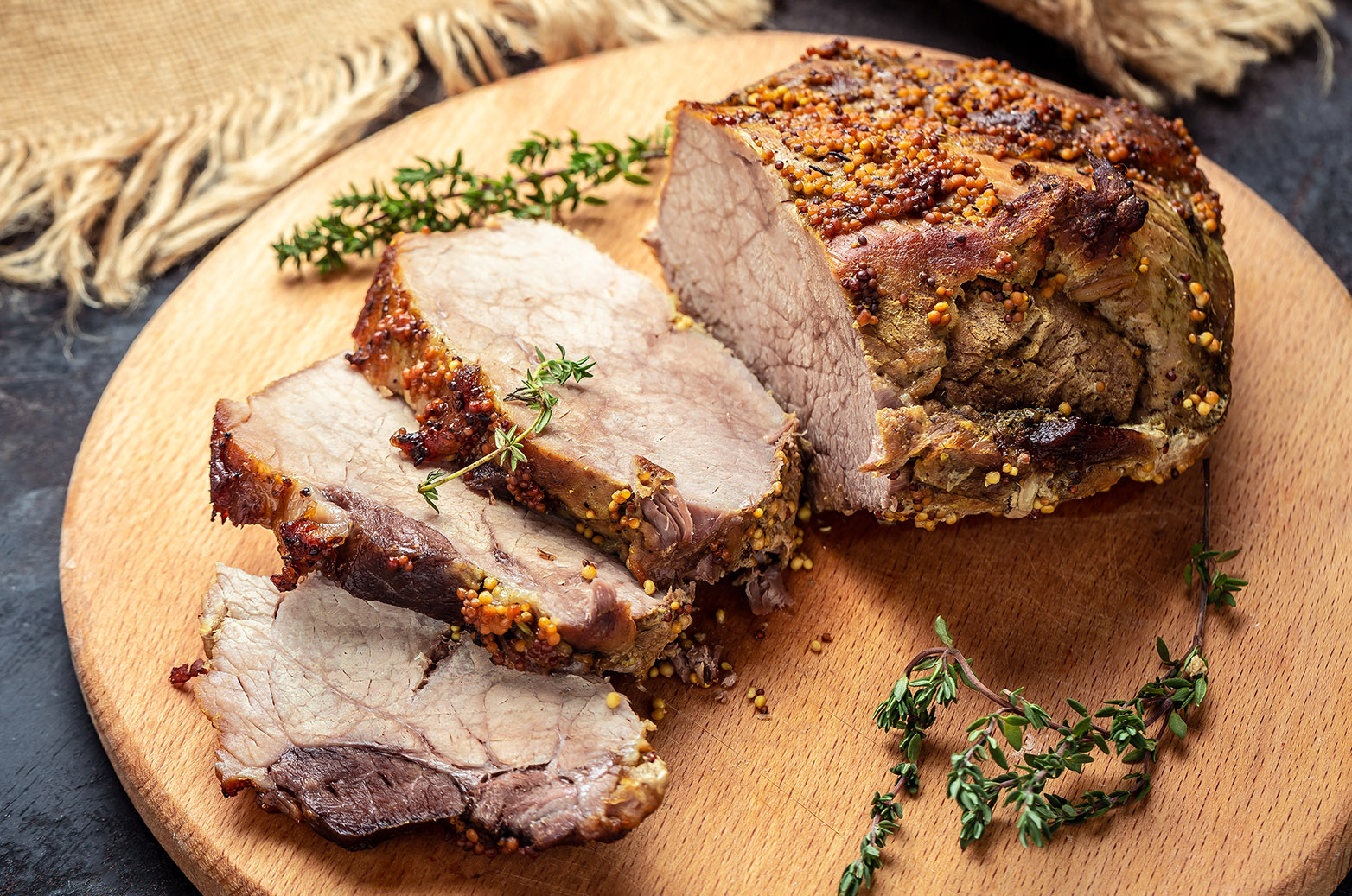 Large sliced piece of baked pork back wwith mustard and thyme on a wooden board. Food recipe background. Close up