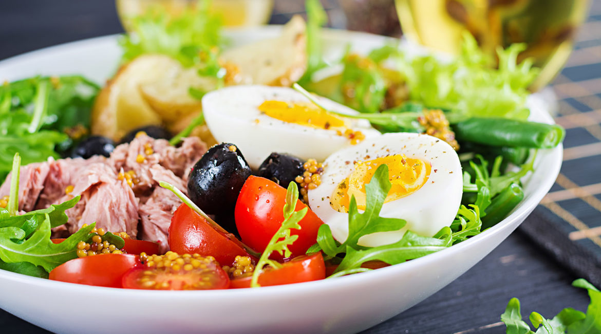 Healthy hearty salad of tuna, green beans, tomatoes, eggs, potatoes, black olives close-up in a bowl on the table. Salad Nicoise. French cuisine.