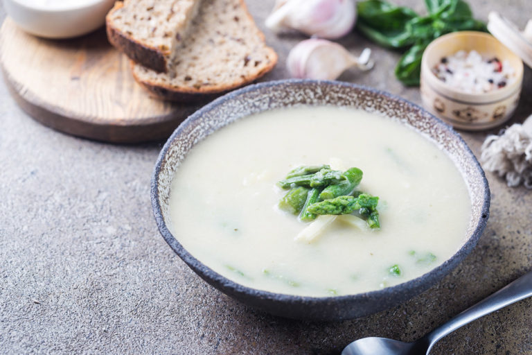 Fresh asparagus cream soup in a bowl over gray stone table